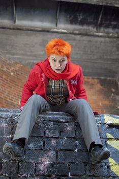 Red-haired woman is sitting on the edge of the wall and looks very surprised