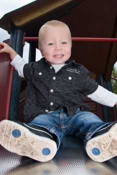 a little boy sitting happily on a shute 