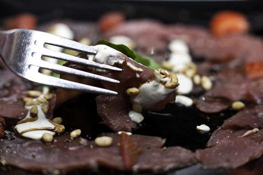 springbok carpaccio with a white sauce, strawberries and nuts on a black plate