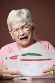 Upset senior woman with many bills and notices