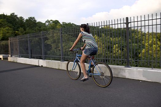 A young woman riding a bicycle across the bridge.