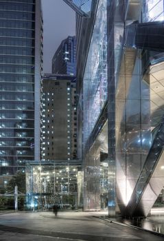Modern skyscraper exterior with businessman walk blurred in night.