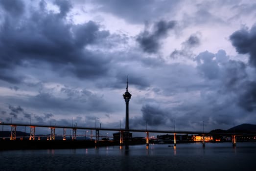 Cityscape in Macao with dramatic clouds and travel tower silhouette in night.