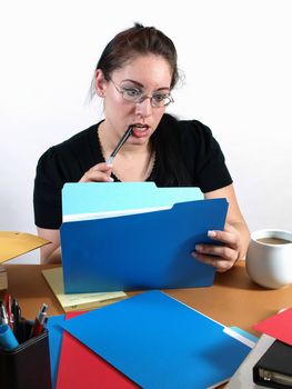 A female office worker checks a file with a pen to her lips.