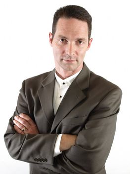 A clean cut man in a business suit stands with his arms folded.