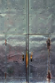 Corroding metal doors of a church.  Door handles are praying angels.
