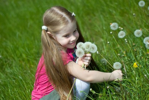 smiling little girl on a green meadow with a bouquet of dandelions