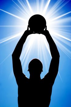 A silhouette of a basketball player holding up a ball in front of a bright glowing lens flare.