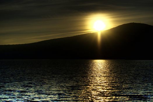 The sun setting over a lake, behind a mountain