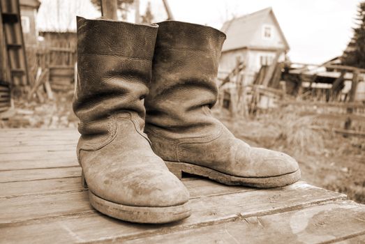 old muddy farmers boots on background wooden wall.tone sepia