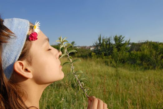 young girl portrait side view smelling a plant on green meadow at summer