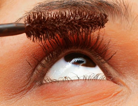 Extreme closeup of a woman's eye, putting makeup on eyelashes 
