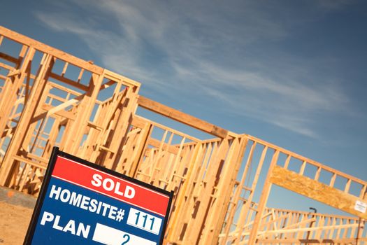 Sold Lot Real Estate Sign at New Home Framing Construction Site Against Deep Blue Sky.