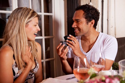 A man giving a ring as a gift to a female in an outdoor cafe