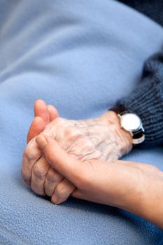 An old handing holding a young hand.  Shallow depth of field with focus on the hands.