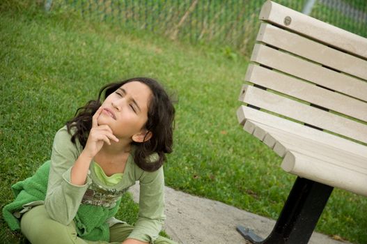 A girl sitting on the ground next to a bench.