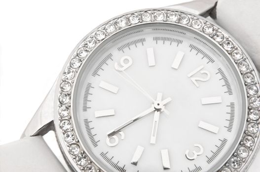 Close up capturing a white and chrome watch face with diamond surround over white.