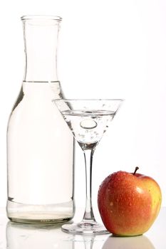 Bottle with transparent water, a glass and apples on a white background