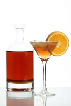 Bottle with an alcoholic drink, a glass and an orange on a white background