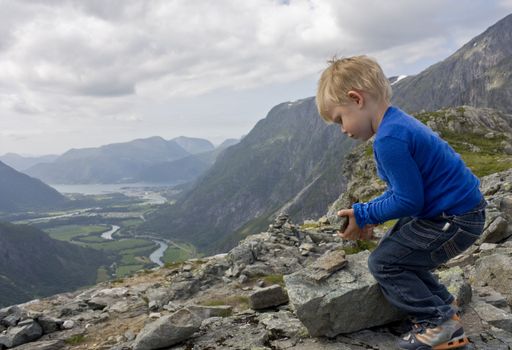 Small boy (3 years old) building a cairn on top of Litjfjellet. �ndalsnes in the background. Rauma, Norway.