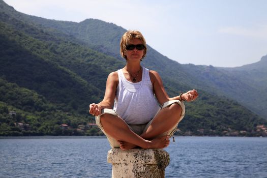The adult woman meditates sitting on a stone
