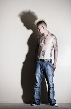 Punk with tattoos leaning against a white wall