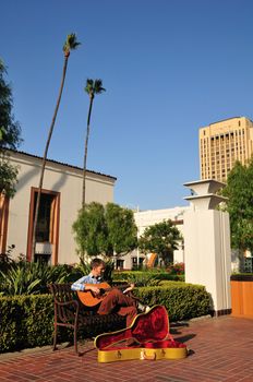 Young man playing guitar for money in a train station courtyard.