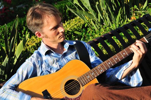 Young man plays guitar outside on a park bench