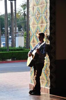 Acoustic guitar player leans against a bright tile doorway