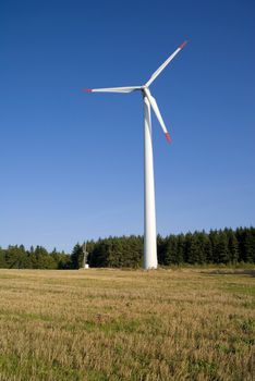 Wind turbine against blue sky with the forest in background