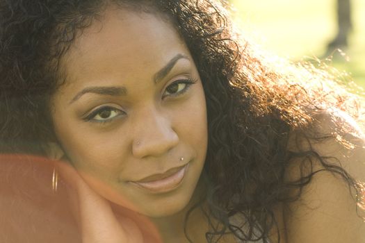 Beautiful portrait of a young black woman laying in grass on a sunny day with sun flare