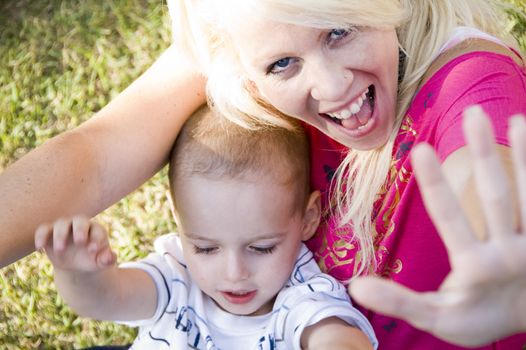 cheerful young woman and little baby sitting on green grass