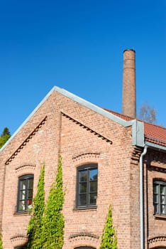 Old factory building on clear polarised blue sky with a chimney behind
