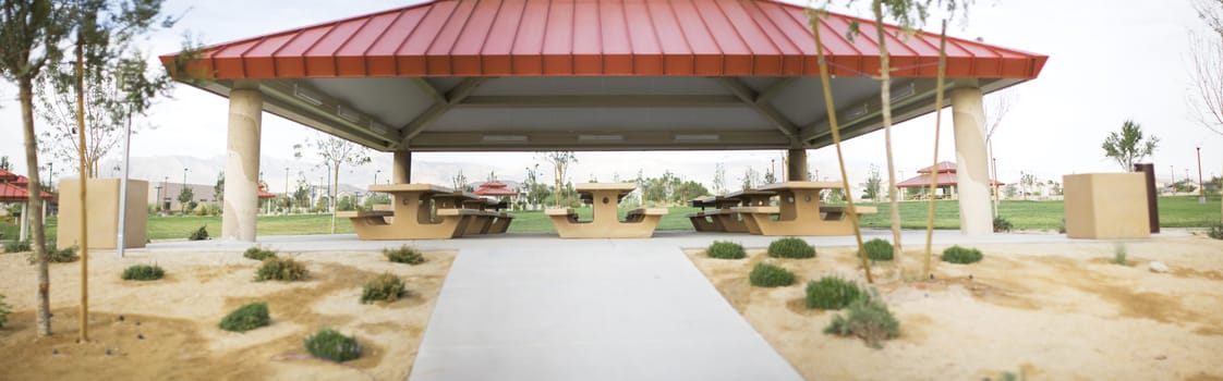 a panoramic of picnic tables and a picnic structure outside in a park with green grass