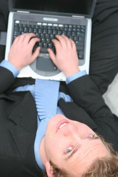 Businessman wearing a blue tie and black suit working on his wireless laptop computer with an overhead view