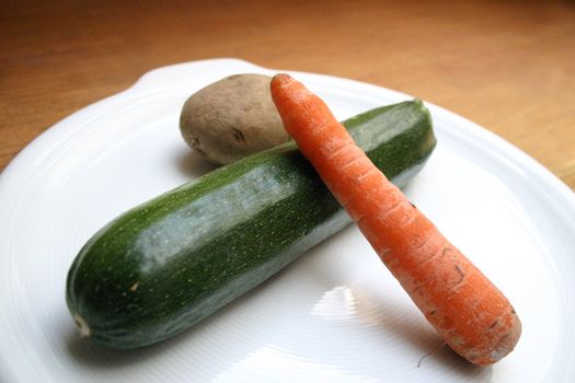 A carrot, cucumber, potato on a white dish