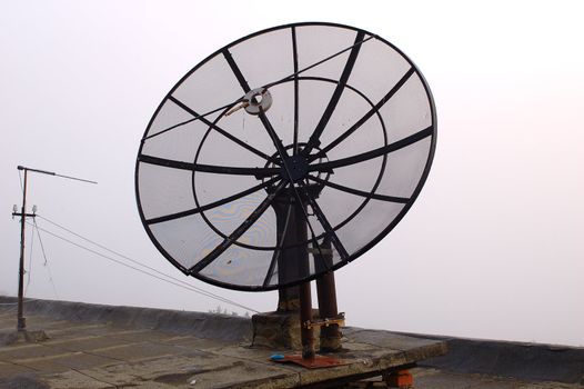 Old black metal rusty satellite antenna on roof.