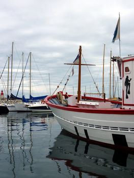 White boat with black painting of a diver diver among other boats floating on the sea by cloudy weather