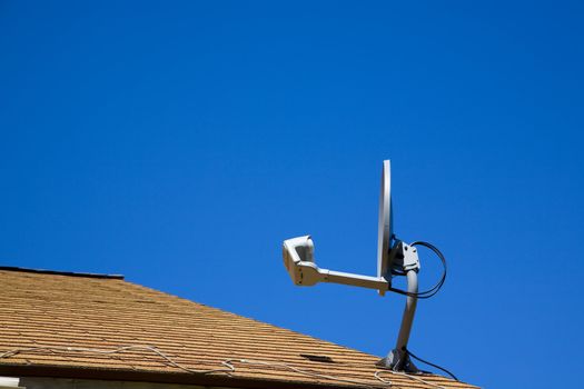 A home satellite dish mounted on a roof against a blue sky.