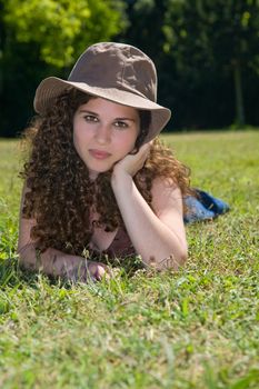 Pretty young girl with a hat, laying down in the grass on a park.