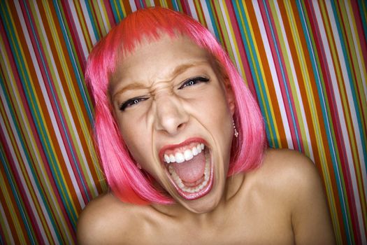 Portrait of attractive Caucasian young adult woman wearing pink wig against striped background making sassy expression at viewer.