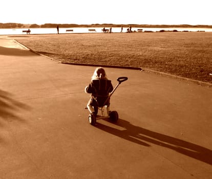 Child riding a tricycle near on a park. Sepia over exposed