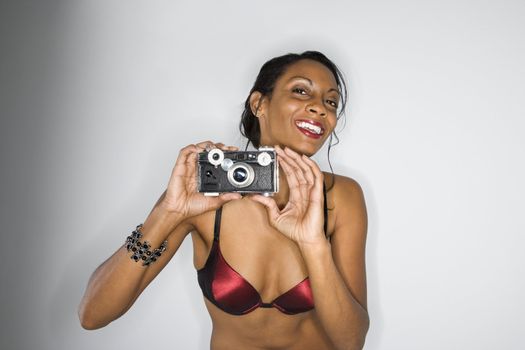 Mid-adult African American woman in bra holding up camera smiling and looking at viewer.