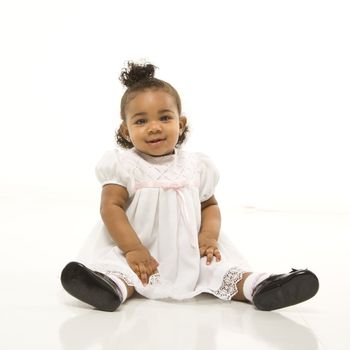 Portrait of African American infant girl sitting against white background.