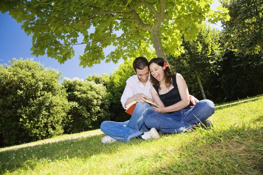 Happy couple laughing while reading a book in a park.