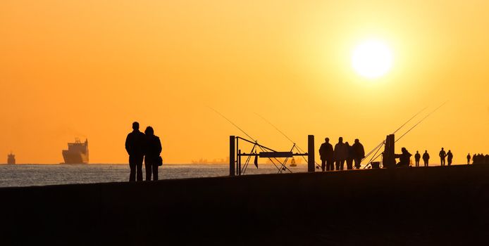 Pier with people fishing and walking - hazy and yellow sunset from volcanodust in the air