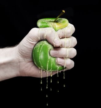 hand to squeeze a green apple isolated in black background