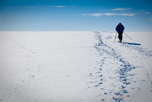 Man cross country skiing towards the horizon. Blue sky with some clouds. Limited DOF. Picture taken in Oppdal, Norway.