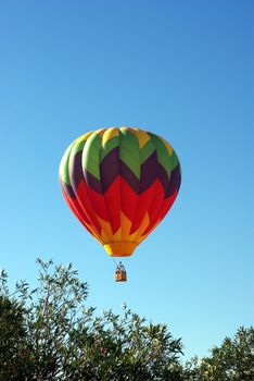 A multi colored Hot Ait Ballon rises into a clear bright sky