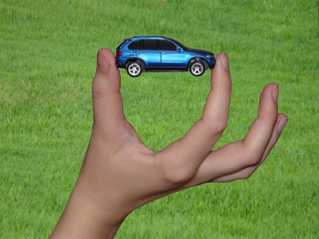 A small car on green background held  by person`s hand